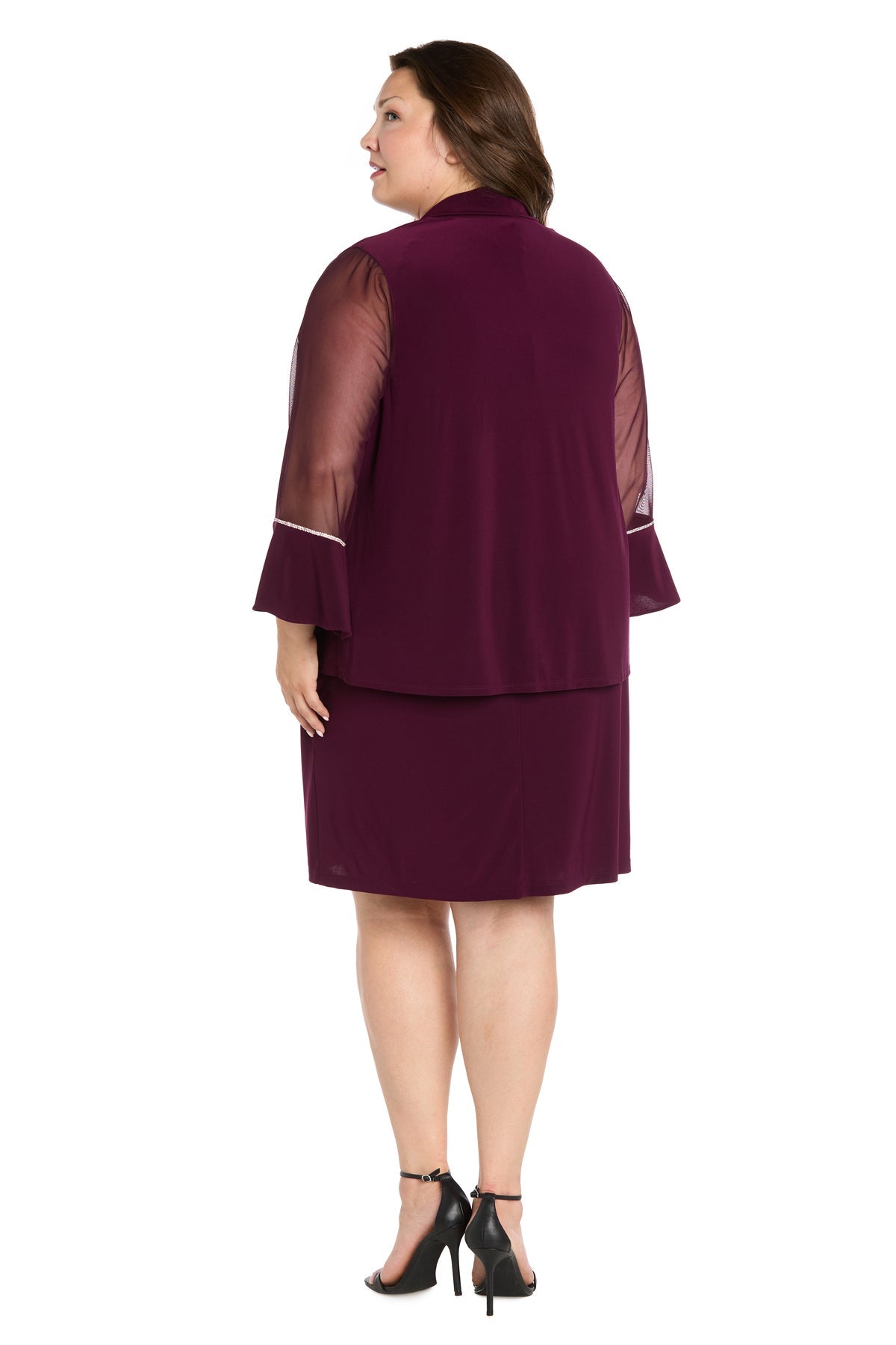 A woman in the Short Plus-Size Jacket Party Dress (R&M Richards 3747W), featuring sheer sleeves and ruffle cuffs, faces away from the camera. She finishes her look with black high-heeled sandals.